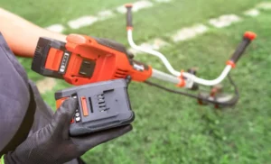 Close up of gardener holding cordless lawn mover and battery