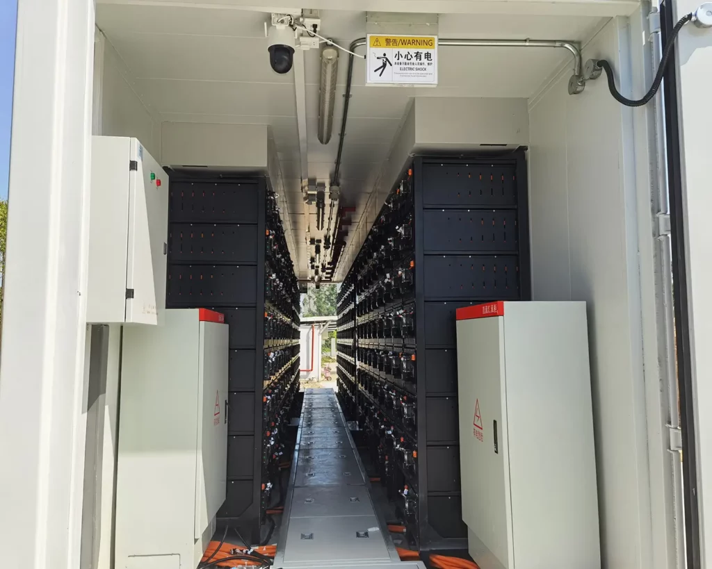 The internal structure of the containerized battery energy storage system consists of rows of black battery rack modules on both sides, and is equipped with transformers, converters, monitoring cabinets, junction boxes, fire protection systems, ducted air conditioning and other facilities.