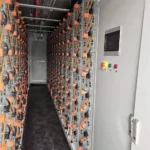 The operation and maintenance channel in the energy storage battery container has many battery modules neatly arranged on both sides, as well as some supporting emergency lighting, alarm lights, monitoring and fire safety systems.